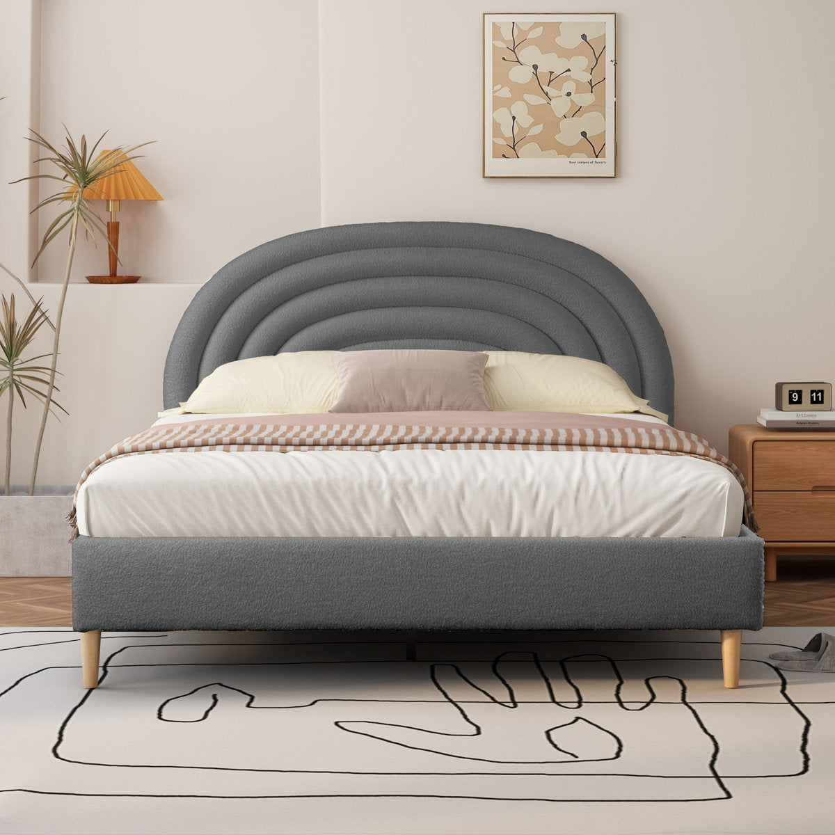 Gray upholstered bed with wooden legs in a bedroom setting.