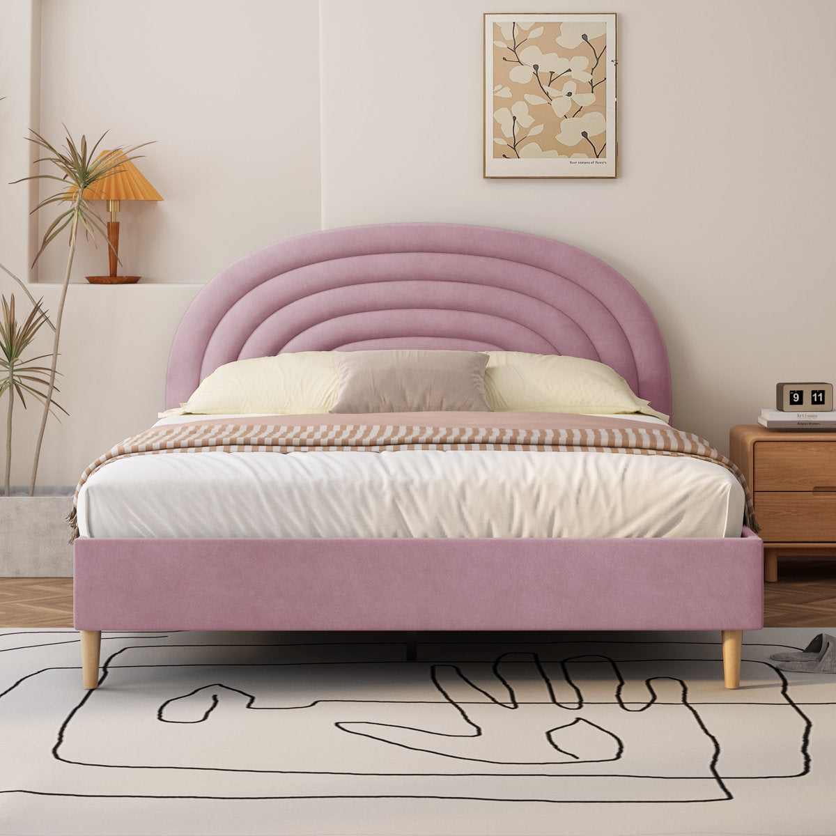 Pink upholstered bed in a bedroom setting with a lamp and artwork on the wall.
