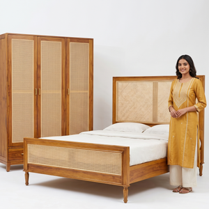 Woman standing next to a wooden bed and wardrobe with wicker detailing.